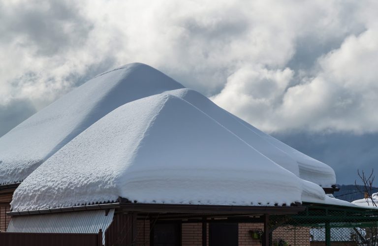 Snow drifts on the roof after the snowfall. In the background, the sky is covered with gray clouds. Roofs of the house, garage and shed in the snow. Three snow pyromids